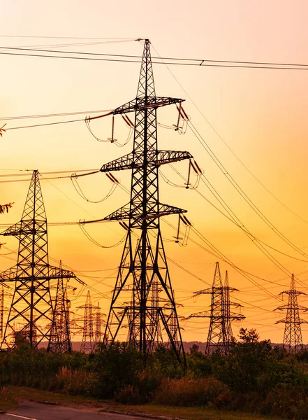 Transmission lines against red evening sky. High-voltage electricity towers at sunset. Silhouettes of electricity pylons and cables at beautiful orange sunset