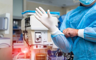 Yetenekli yakışıklı doktor modern klinikte hasta ameliyat ediyor. Erkek cerrah ameliyata hazırlanırken önlüğünü giyiyor.