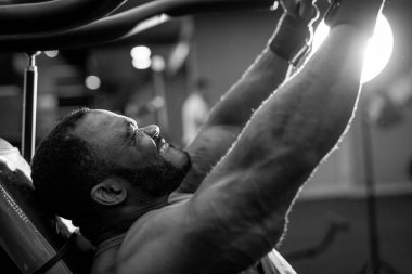 Güçlü atletik vücut geliştiricisinin dambılla egzersiz yaparken çekilmiş siyah beyaz bir fotoğrafı. Spor salonunda fitness kaslı çok ırklı adam eğitimi. Fitness konsepti