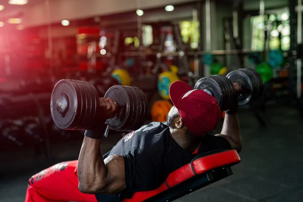 Strong african man in a gym. Handsome man with big muscles feeling confident while training hard at the dark gym. Stock photo