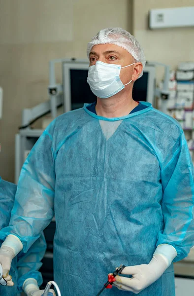 Confident surgeon wearing protective mask holding special equipment and working during the operation at the patient. Medicine concept