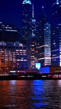 New York, USA, 1 August 2025: Many the waterfront of the East River. Beautiful buildings of Manhattan with lights on in the windows. View of New York from the river at night. Vertical video.