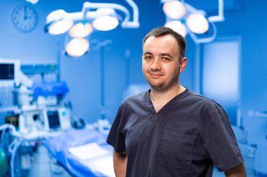 Hastanedeki erkek doktorun portresi. Ameliyat odasında poz veren önlüklü bir erkek doktor. Arka planda ameliyat ışıkları var..