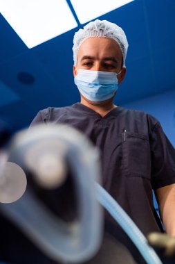 Ameliyathanede koruyucu maskeli bir cerrah. Tıbbi maske takan bir cerrah ameliyathanede ameliyata hazırlanıyor..