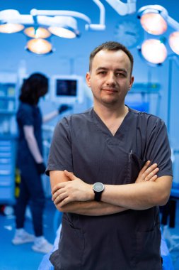 Ameliyathanede kolları bağlı bir erkek cerrah. Kolları bağlı bir erkek cerrah ameliyata hazırlanırken ameliyathanede duruyor..