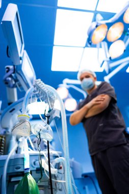 Anestezi uzmanı ameliyathanede ekipman hazırlıyor. Koruyucu giysiler giyen bir erkek anestezi uzmanı ameliyattan önce anestezi malzemeleri hazırlar..