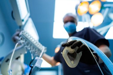 Anestezi maskeli doktor ameliyathanede. Koruyucu eldiven giyen doktor ameliyathanede anestezi maskesi tutuyor..