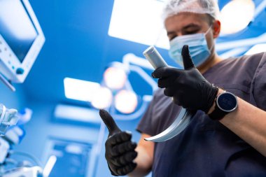 Cerrah ameliyathanede laringoskop hazırlıyor. Koruyucu maskeli doktor ve eldivenli eldiven hastane ameliyathanesinde laringoskop aleti tutuyor..