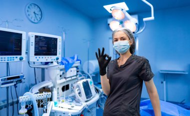 Kadın anestezi uzmanı ameliyathanede iyi niyet gösteriyor. Maskeli ve eldivenli gülümseyen anestezi uzmanı modern hastane ameliyathanesinde iyi hareket ediyor..