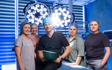 Ameliyathanede tıbbi ekibi olan bir cerrah var. Cerrah ve hemşirelerin bir ameliyathanede cerrahi önlüklerle yan yana durdukları grup portresi..