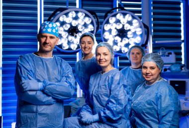 Ameliyathanede tıbbi ekip portresi. Modern bir ameliyathanede birlikte duran mavi önlüklü cerrahların ve hemşirelerin grup fotoğrafı..