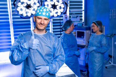 Cerrah ameliyathanede onay veriyor. Önlüklü ve şapkalı cerrah, arka planda ekibin olduğu parlak bir ameliyathanede onay verdi..