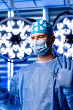 Ameliyattan önce ellerini kaldırmış bir cerrah. Koruyucu giysili ve maskeli cerrah ameliyat öncesi el kaldırdı..