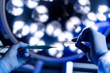 Ameliyathanede doktorların kullandığı cerrahi aletler. Steril ortamda ameliyat ışıkları altında cerrahi aletler tutan doktorların yakın çekimleri.
