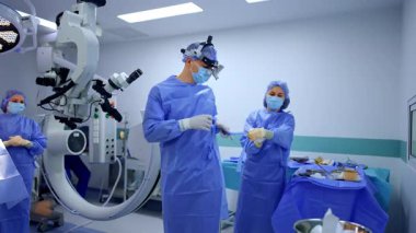 Orta yaşlı, beyaz erkek cerrah ameliyat için giyiniyor. Kadın doktor ameliyattan önce doktora yardım ediyor.