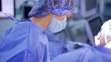 Mavi şapkalı, maske ve bornozlu beyaz kadın doktor. Nöroşirürjide asistanlık yapan bir hemşirenin portresi. Bulanık arkaplan.