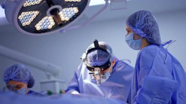 Cerrahi loupes 'taki doktor çok sıkı çalışıyor. Kadın ameliyat hemşireleri nörocerrahın ameliyatına yardım eder..