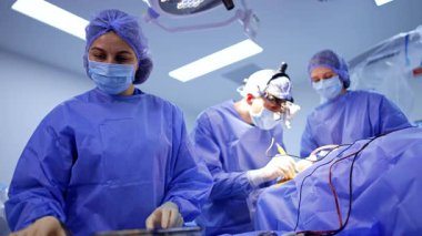 Mavi bornozlu kadın doktor cerrahi standında duruyor. Hemşire, ameliyatta çalışan beyin cerrahı için bir alet hazırlıyor. Düşük açı görünümü.