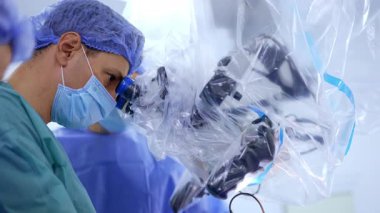 Odaklanmış beyaz erkek cerrah mikroskop dürbününe bakar. Modern beyin cerrahisi yapan bir doktorun yan görüş portresi.