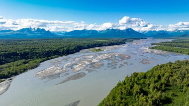 Alaska 'nın el değmemiş havası manzarasında örülmüş bir nehir. Parlak mavi gökyüzünün altında, ormanlar ve uzak dağ tepeleriyle çevrili örülmüş nehrin hava görüntüsü..