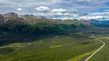 Alaska 'da dağların olduğu bataklık ve orman manzaralı. Alaska 'nın yeşil ormanlık, göletli ve bulutlu gökyüzünün altındaki uzak dağların drone görüntüsü..