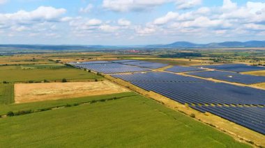 Yeşil alanlara fotovoltaik hücreler yerleştirildi. Yerleşim alanı, sıradağlar ve arka planda bulutlu gökyüzü.