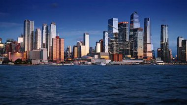 New York 'un ufuk çizgisindeki binaların çeşitli stili, tasarımı ve boyutları. Gün batımında nehir manzarasından şehre bak..