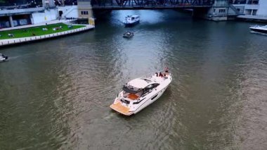 Chicago, ABD, 29 Haziran 2025, Chicago Nehri 'ndeki tekneler köprüye gidip geliyor. İnsanlar rıhtımdaki çimlerde dinleniyor..