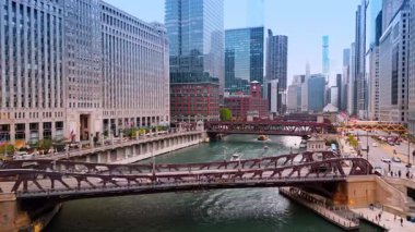 Şikago, ABD, 29 Haziran 2025: Şikago Nehri manzarası çarpıcı binalarla çevrili. İnsanlar ve arabalar nehrin karşısındaki köprülerden geçiyor. Tekneler köprünün altından geçer..