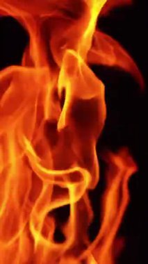 Karanlıkta hareket eden kırmızı ve sarı alevlerin dilleri. Küçük kıvılcımlar havada uçuşuyor. Kapatın. Dikey video