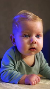 Şaşkınlıkla etrafa bakan şirin bir bebek. Sevimli çocuk kameranın önünde yüzüstü yatıyor. Kapatın. Dikey video