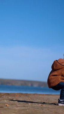 Kafkasyalı bir çocuk yerde bir taş yığınının yanına geldi. Çocuk bir taş aldı ve atmak için suya koştu. Düşük açı. Dikey video