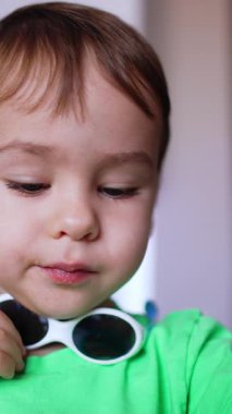 Boynuna güneş gözlüğü takmış, kendini yiyen beyaz bir çocuk. Yemek yiyen sevimli bir çocuğun portresi. Kapatın. Dikey video