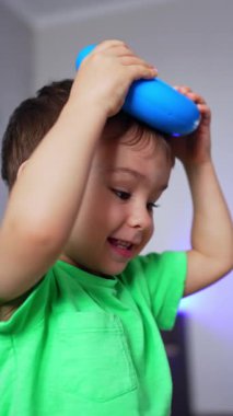 Açık mavi tişörtlü şirin çocuk oyuncak piramidin yüzüğünü kafasına takıyor. Mutlu çocuk evde eğleniyor. Arkaplan bulanık. Dikey video