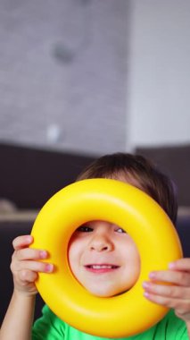 Tatlı bebek oyuncak piramidin sarı halkasına bakıyor. Çocuk kameraya gülümserken kafasına koyuyor. Düşük açı. Dikey video