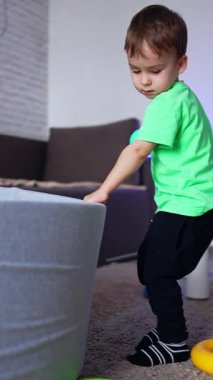 18 aylık bir bebek, kuru havuzlu bir odada oynuyor. Küçük çocuk havuza bir top attı. Dikey video