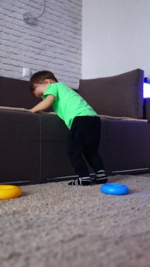 Kanepede neşeli bir şekilde zıplayan enerjik bir beyaz çocuk. Küçük çocuk kameraya yaklaşırken pantolonunu yukarı çekiyor. Düşük açı. Dikey video