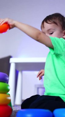 Sakin şirin çocuk yerde oturmuş piramit kuruyor. Evde oynayan çocuğun düşük açılı görüntüsü. Dikey video