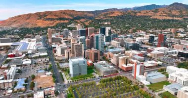 Dikilmiş ağaçlarla dolu yeşil bir otopark arasında mesafe var. Yollarda çok sayıda araç var. Arka planda yerleşim alanlarıyla kaplı kayalar. Salt Lake City, Utah, ABD. Hava görünümü.