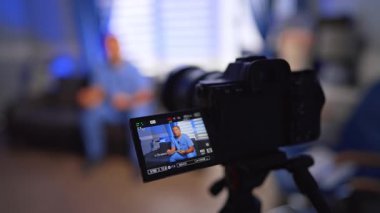 Modern kamera tıbbi bir vlog kaydediyor. Kapatın. Mavi üniformalı adam kanepede oturup video için konuşuyor. Seçici odak.