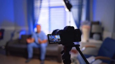 Kamera, kanepede oturup video içeriği hakkında konuşan bir adamın video bloğunu kaydediyor. İçerik oluşturan bir erkek vlogger üzerine seçici odak.