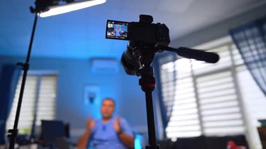 Mavi üniformalı konuşan bir adamın videosunu çeken bir tripodun kamera görüntüsü. Düşük açı. Modern vlog konsepti. Seçici odak.