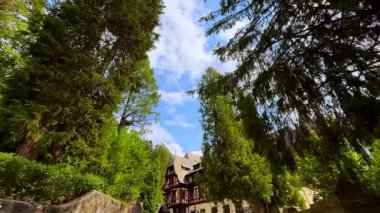 Yeşil ağaçlar boyunca yürüyüp güzel binaya yaklaşıyoruz. Romanya 'nın Sinaia kentindeki Peles Kalesi' nin düşük açılı manzarası.