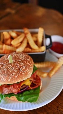 Klasik çizburger, kola ve beyaz tabakta patates kızartması. Peynirli ve ketçaplı taze çizburger. Tahta masada patates kızartması ve kola ile servis ediliyor..