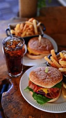 Kırsal ahşap masada patates kızartması ve soda ile klasik çizburger. Taze çizburger, patates kızartması ve kola. Kafe ortamında sıcak ışık altında..