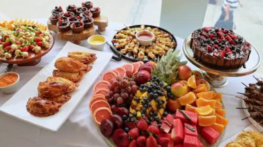 Tatlı, meyve ve abur cuburlarla süslü büfe masası. Parti ya da etkinlik için beyaz masa örtüsü üzerinde meyveler, pastalar, pastalar ve aperatiflerle servis kurulumu.