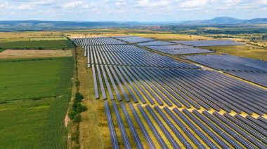 Ufukta dağlar olan güneş çiftliği manzarası. Uzaktan görülebilen dağ sıraları olan geniş bir güneş paneli çiftliğinin havadan görüntüsü..