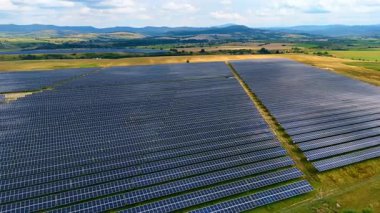 Yeşil alanlar ve güneş panellerinden oluşan hava manzarası. Yeşil tarım arazileri ve vadileri boyunca uzanan güneş panellerinin insansız hava aracı görüntüleri.