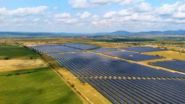 Güneş enerjisi alanı tarım arazileriyle çevrili. Mavi gökyüzünün altında tarımsal tarlalarla çevrili büyük bir güneş çiftliğinin insansız hava aracı görüntüsü..