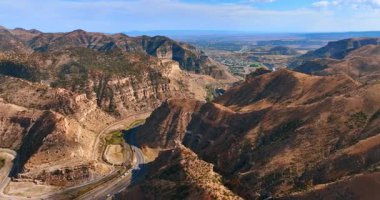 Utah 'taki Fiyat Kanyonu' nun virajlı yolu ve parlak gökyüzünün altındaki katmanlı dağ kayalıkları..